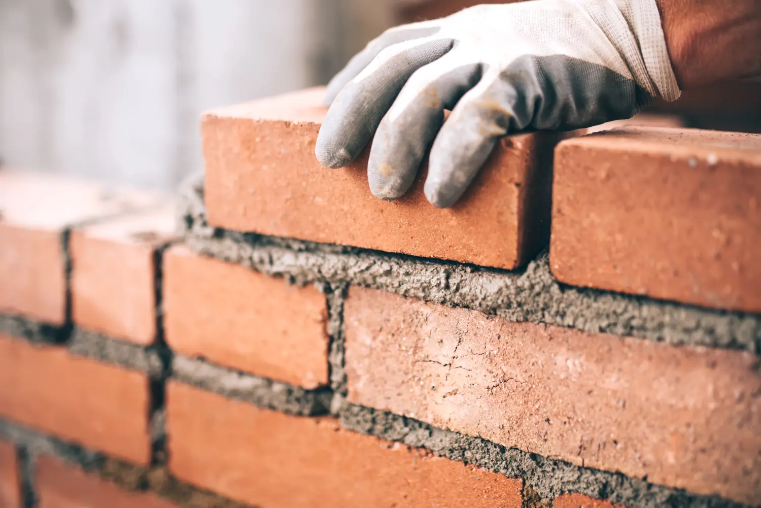 Nahaufnahme eines industriellen Maurers, der auf einer Baustelle Ziegelsteine verlegt