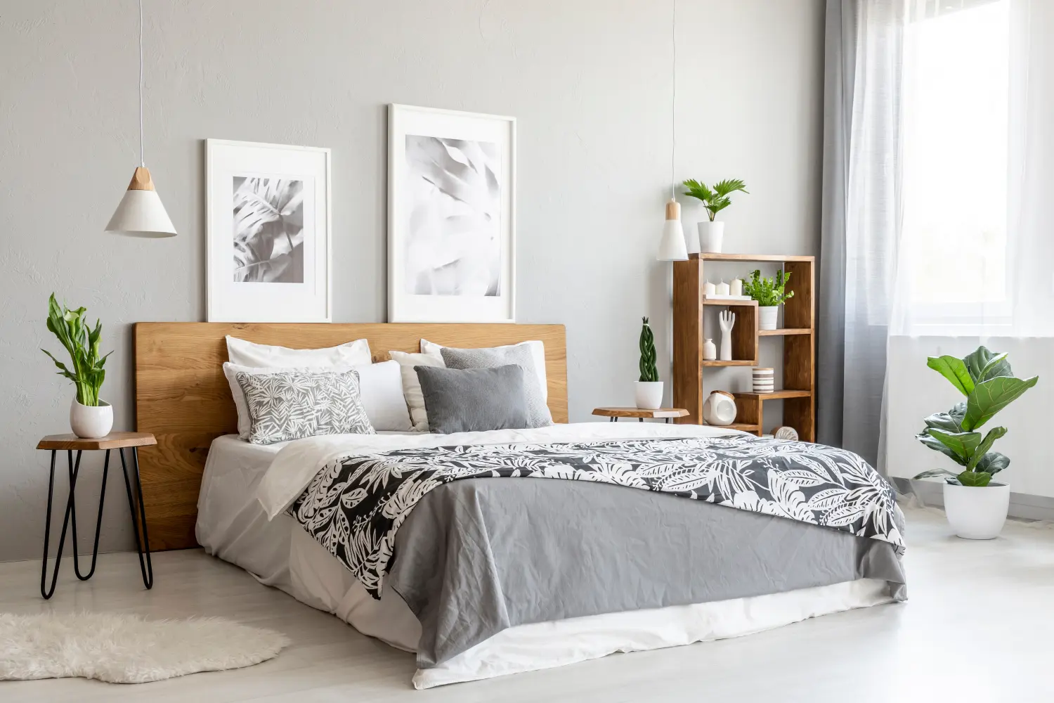 Gemusterte Decke auf Holzbett in grauem Schlafzimmerinterieur mit Pflanzen und Postern. 
