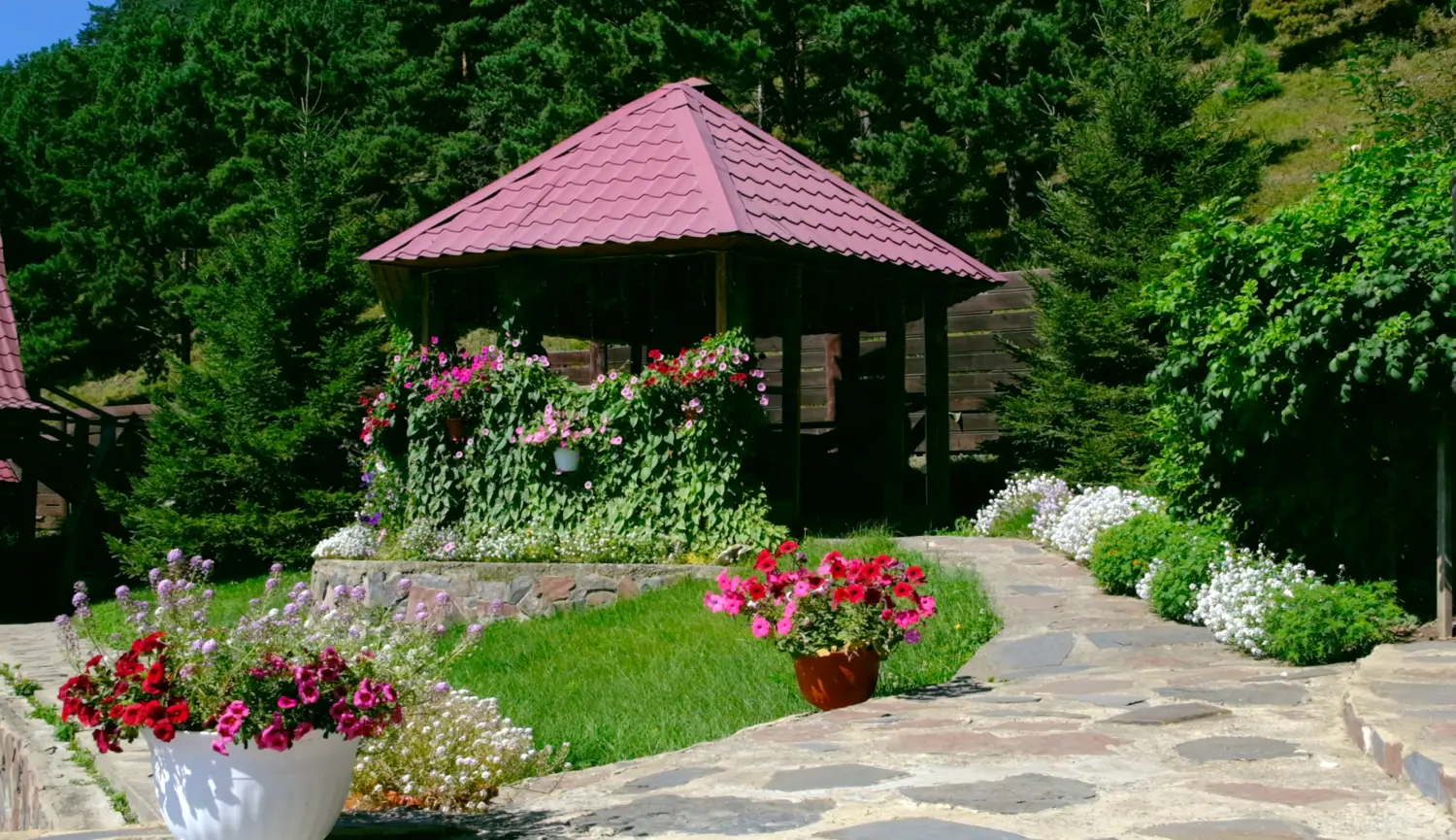 Gepflegter Garten mit Terrasse, Holzpavillon und Veranda mit Sommerblumen. Hütte und Urlaub, Berghotel Resort
